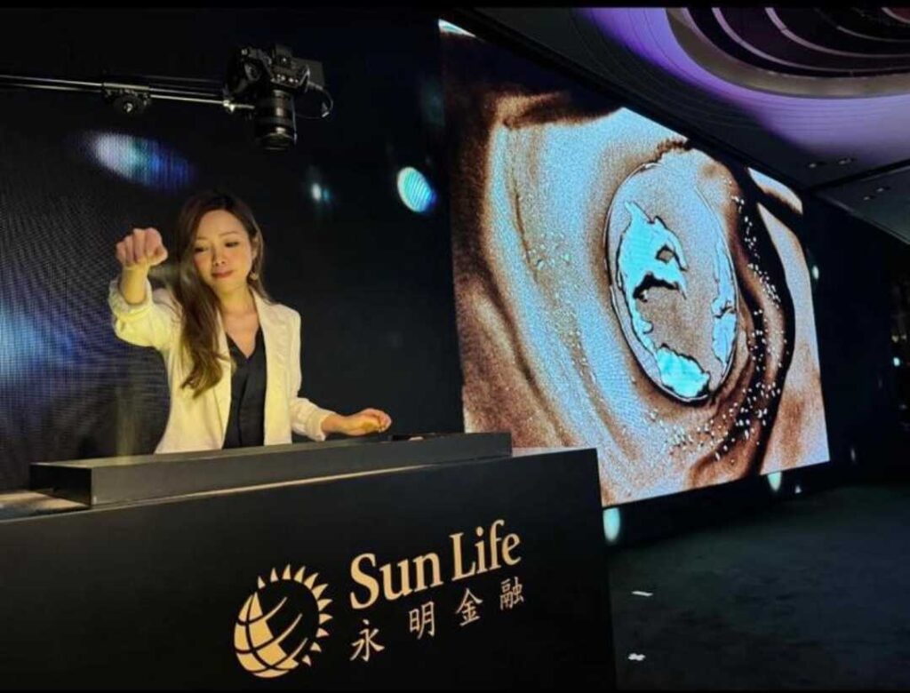 在香港的藝術界,鍾雪是一位別具一格的創作者。她不是用畫筆,而是用沙子,把一個又一個動人的故事呈現在觀眾眼前。從2015年開始,她不只是一位沙畫藝術家,更是一位推動者,她成立了香港沙畫協會、創辦全球首個沙畫體驗館,並領導全港第一個分級考核沙畫證書學院。這一切的起點,源於她對故事的熱愛和對沙畫無限可能的堅信。