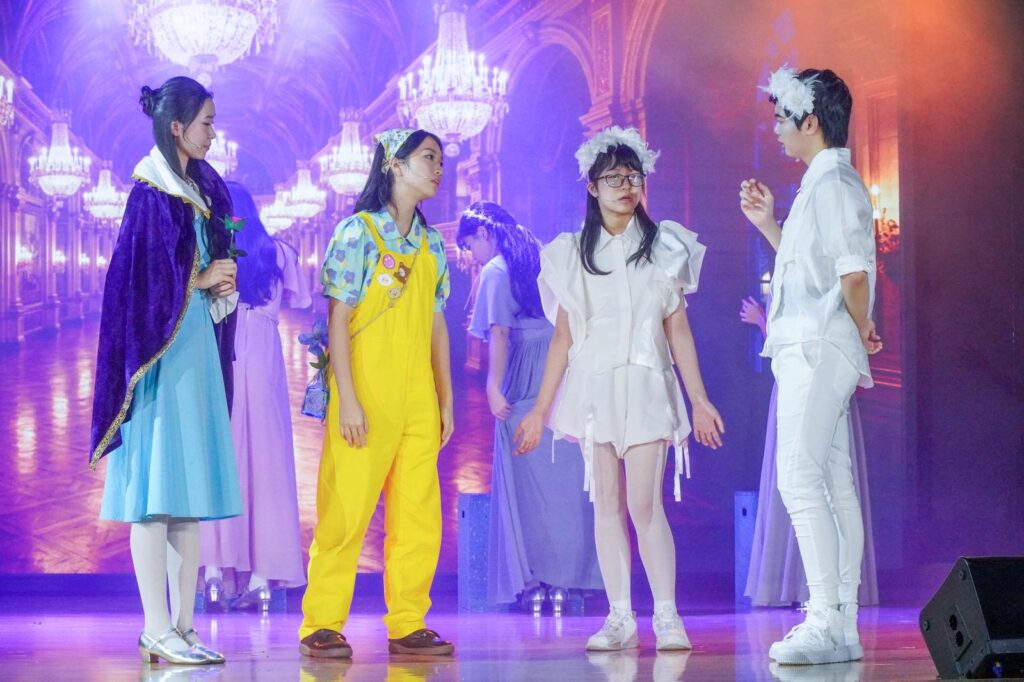 不是每一種學習都能在課室裡完成。有些能力，包括：自信、合作、承擔、面對壓力時的穩定，都需要一個更真實的場景，一群人為同一件事努力，彼此補位，然後在燈光亮起的一刻，把成果交給觀眾。鐘聲慈善社胡陳金枝中學多年來把音樂劇當作校園文化的一部分，並非為了「做一場表演」，而是刻意為學生創造一種獨特的成功感：讓他們在台前台後都能找到位置，感受到自己被需要、能做到、做得到。音樂劇也因此成為一種活動式學習——把語言、情感、價值觀與團隊精神，放進同一個具體而熱烈的練習場。