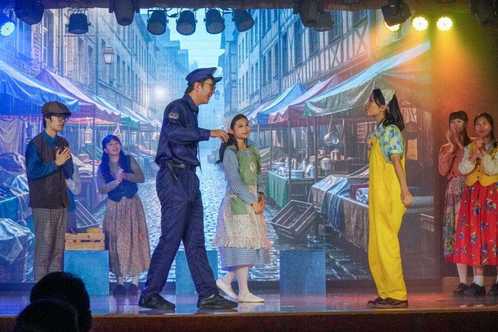 不是每一種學習都能在課室裡完成。有些能力，包括：自信、合作、承擔、面對壓力時的穩定，都需要一個更真實的場景，一群人為同一件事努力，彼此補位，然後在燈光亮起的一刻，把成果交給觀眾。鐘聲慈善社胡陳金枝中學多年來把音樂劇當作校園文化的一部分，並非為了「做一場表演」，而是刻意為學生創造一種獨特的成功感：讓他們在台前台後都能找到位置，感受到自己被需要、能做到、做得到。音樂劇也因此成為一種活動式學習——把語言、情感、價值觀與團隊精神，放進同一個具體而熱烈的練習場。